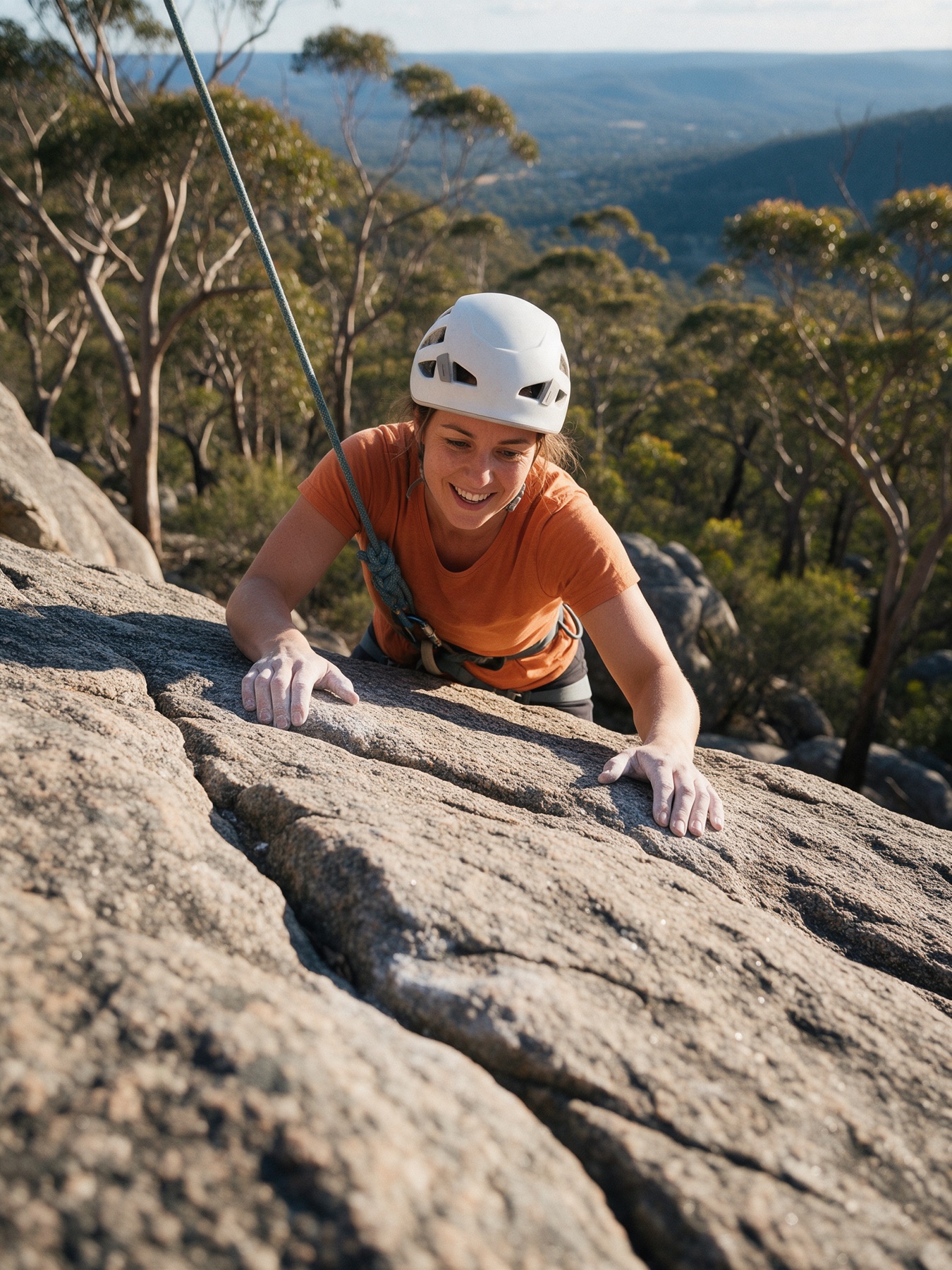 A smiling woman on a top rope looks down at the camera, with a Perth Hills valley behind her.
